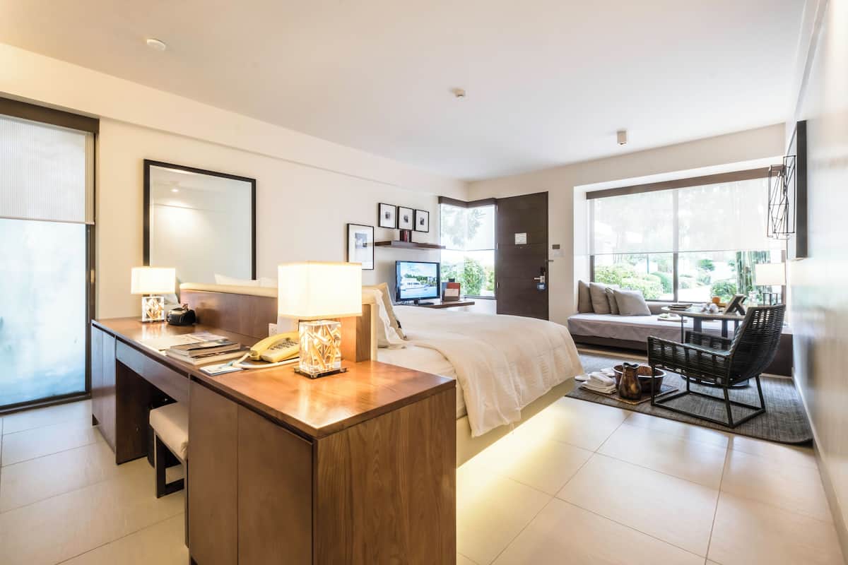 A modern hotel room with a desk, bed, sofa, and dining area.