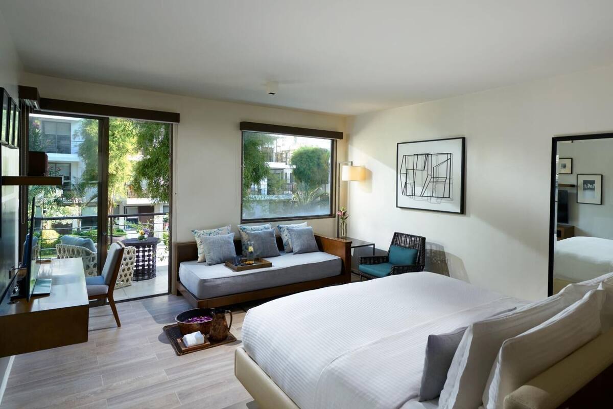 A hotel room with a bed, seating area, a dining table, and a large window.