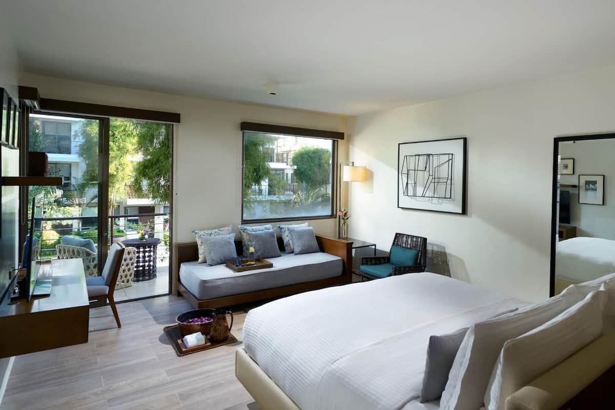 Habitación de hotel con cama, zona de estar, mesa de comedor y un amplio ventanal.