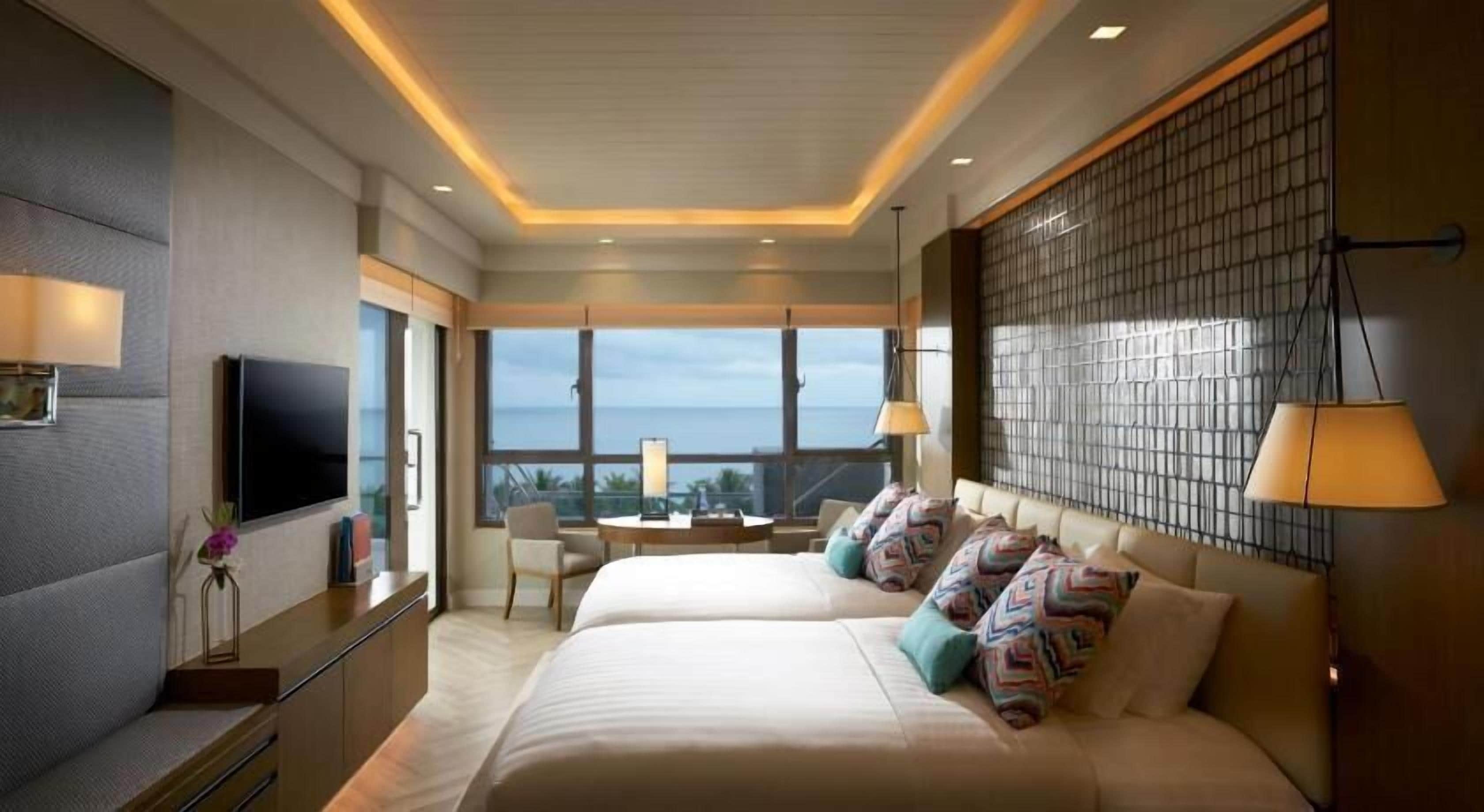 Habitación de hotel con dos camas, televisión, escritorio y vista al océano.