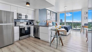 A modern kitchen with stainless steel appliances, a dining area with a glass table, and a large balcony with a city view.