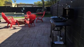 Un patio trasero con una parrilla, sillas rojas y una pequeña mesa.