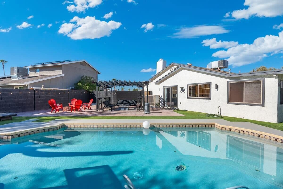 A swimming pool with a patio area, a covered seating area, and a white building with a garage.