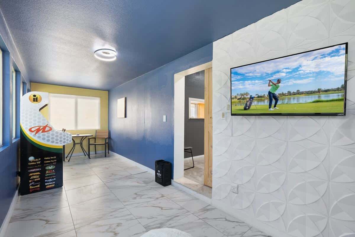 Un interior moderno con un televisor de pantalla plana mostrando una escena de golf, una máquina expendedora y una puerta que da a otra habitación.