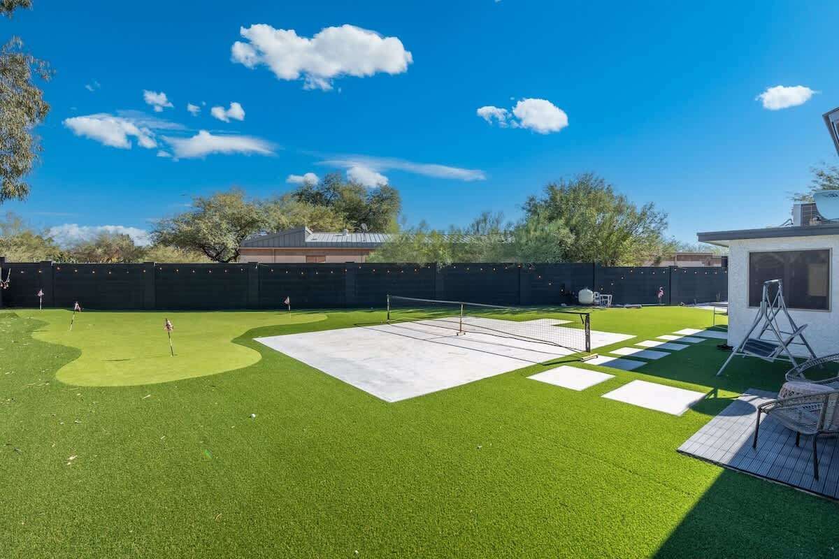 A backyard with artificial grass, a tennis court, and a small white structure.
