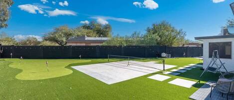 A backyard with artificial grass, a tennis court, and a small white structure.