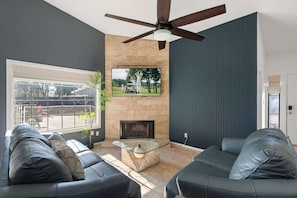 Una sala de estar moderna con chimenea, ventilador de techo y un ventanal grande.