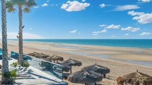 A beach view with palm trees, a pool area, and thatched umbrellas. - Encantame Towers | Ground Floor| Lazy River| Pool (Playa Encanto)