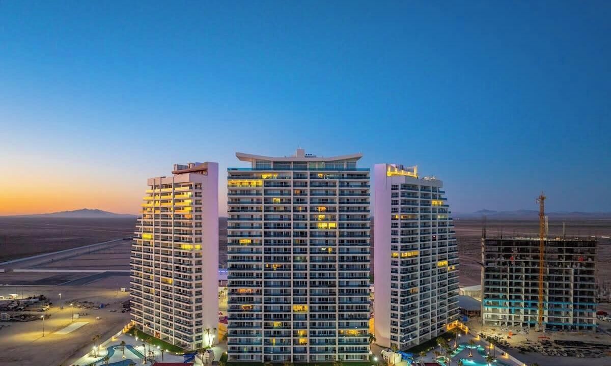 Un hôtel de grande hauteur, avec de nombreux étages, une piscine et un paysage désertique en arrière-plan.