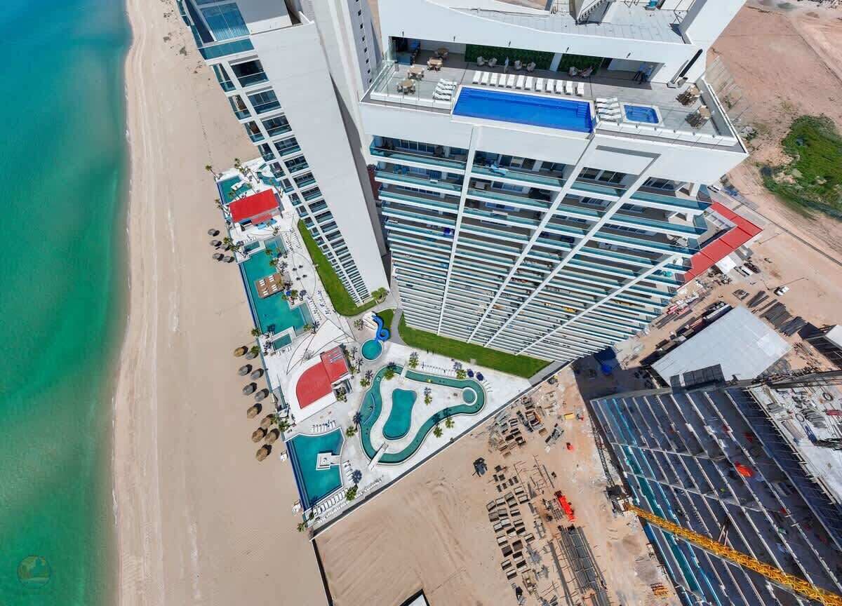 A high-rise hotel with a rooftop pool, adjacent to a beach.