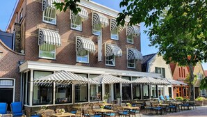 A traditional brick building with a cafe area featuring outdoor seating and striped awnings.
