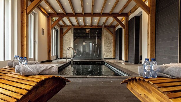 A spa area with a wooden bench seating, a pool, and a stone wall in the background.