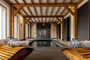 A spa area with a wooden bench seating, a pool, and a stone wall in the background. - Boutique hotel Badhotel Bruin (Vlieland)