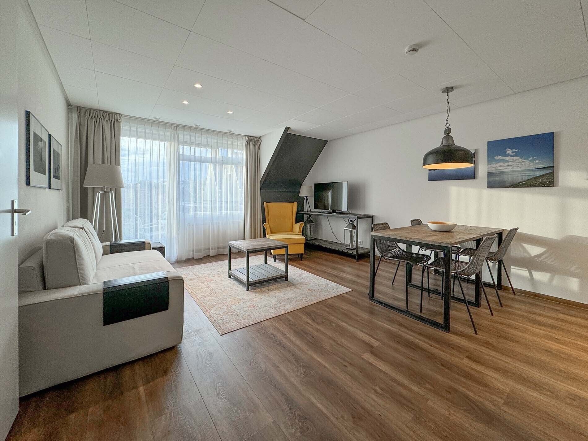 A modern living room with a sofa, a dining table with chairs, a TV, and a lamp.