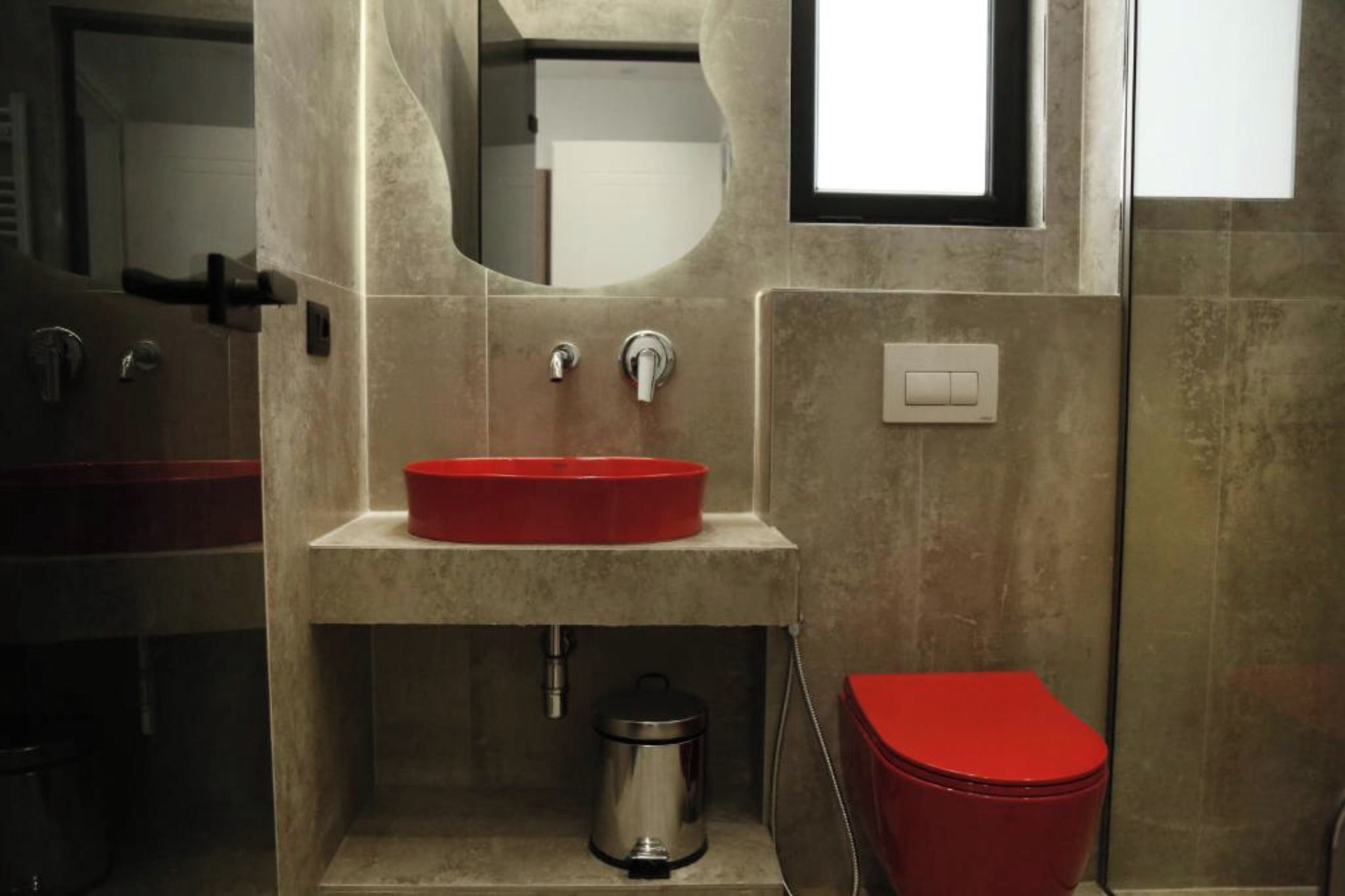 Een badkamer met een rode wasbak, een rood toilet en een spiegel.