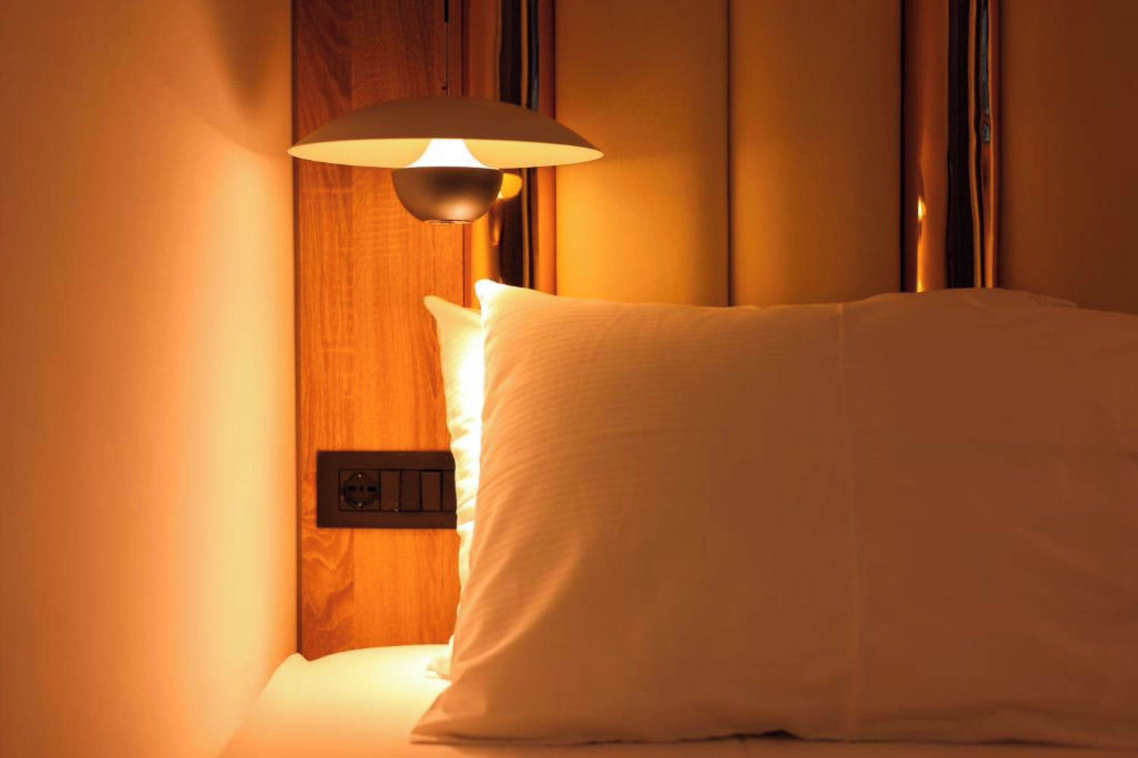 A hotel room with a bed, a wall-mounted light fixture, and a power outlet.