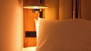 A hotel room with a bed, a wall-mounted light fixture, and a power outlet.