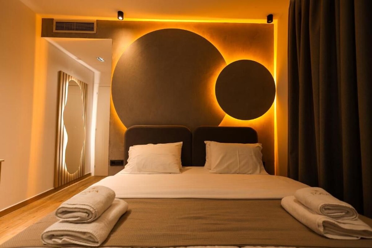 A hotel room with a large bed, two pillows, a headboard with circular light fixtures, and a towel on the bed.