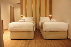 Habitación de hotel con dos camas, suelo de madera y un panel de pared de madera vertical.