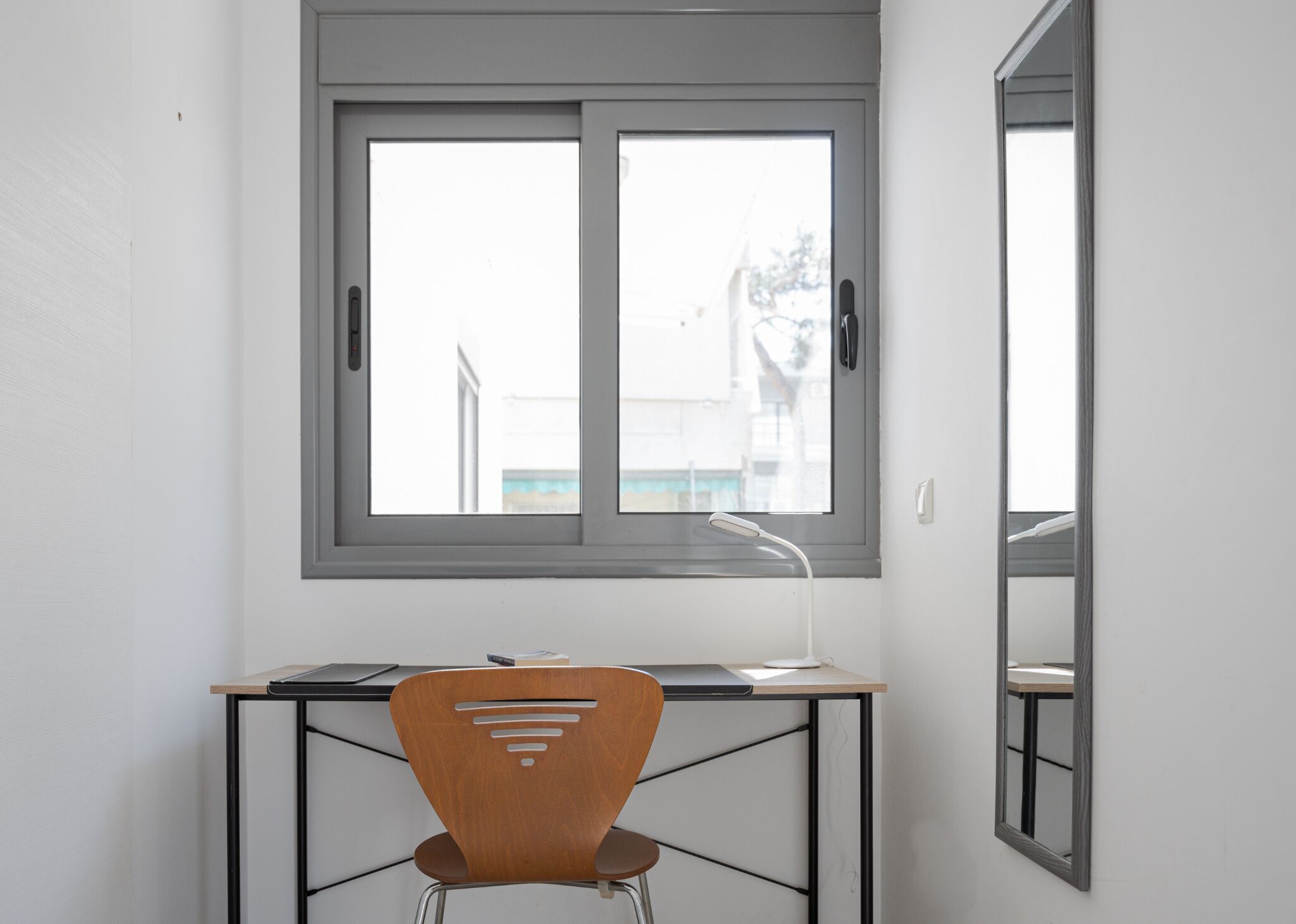 Een kamer met een bureau, stoel en raam met uitzicht op gebouwen.