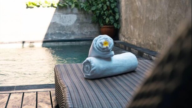 A wooden deck with a wicker lounge chair and a rolled towel with a flower.