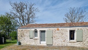 A stone building with a tiled roof, two windows with shutters, and a door.