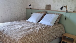 A bedroom with a bed, two bedside lamps, a nightstand, and a wooden shelf above the bed.