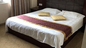 Una cama con ropa de cama blanca y dorada, un cabecero y una mesita de noche.