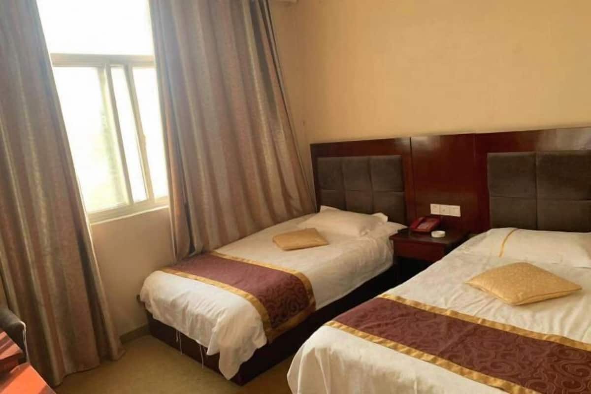 Habitación de hotel con dos camas, una mesita de noche, un teléfono y una ventana con cortinas.