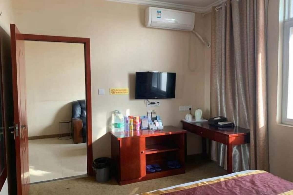 Habitación de hotel con cama, televisor, escritorio con silla, un pequeño rincón de descanso y un equipo de aire acondicionado.