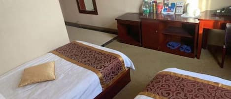 Ein Hotelzimmer mit zwei Einzelbetten, einem Schreibtisch mit Stuhl, einem Fernseher und einem Schuhregal.