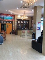 A hotel lobby with a reception desk, seating area, and a chandelier.