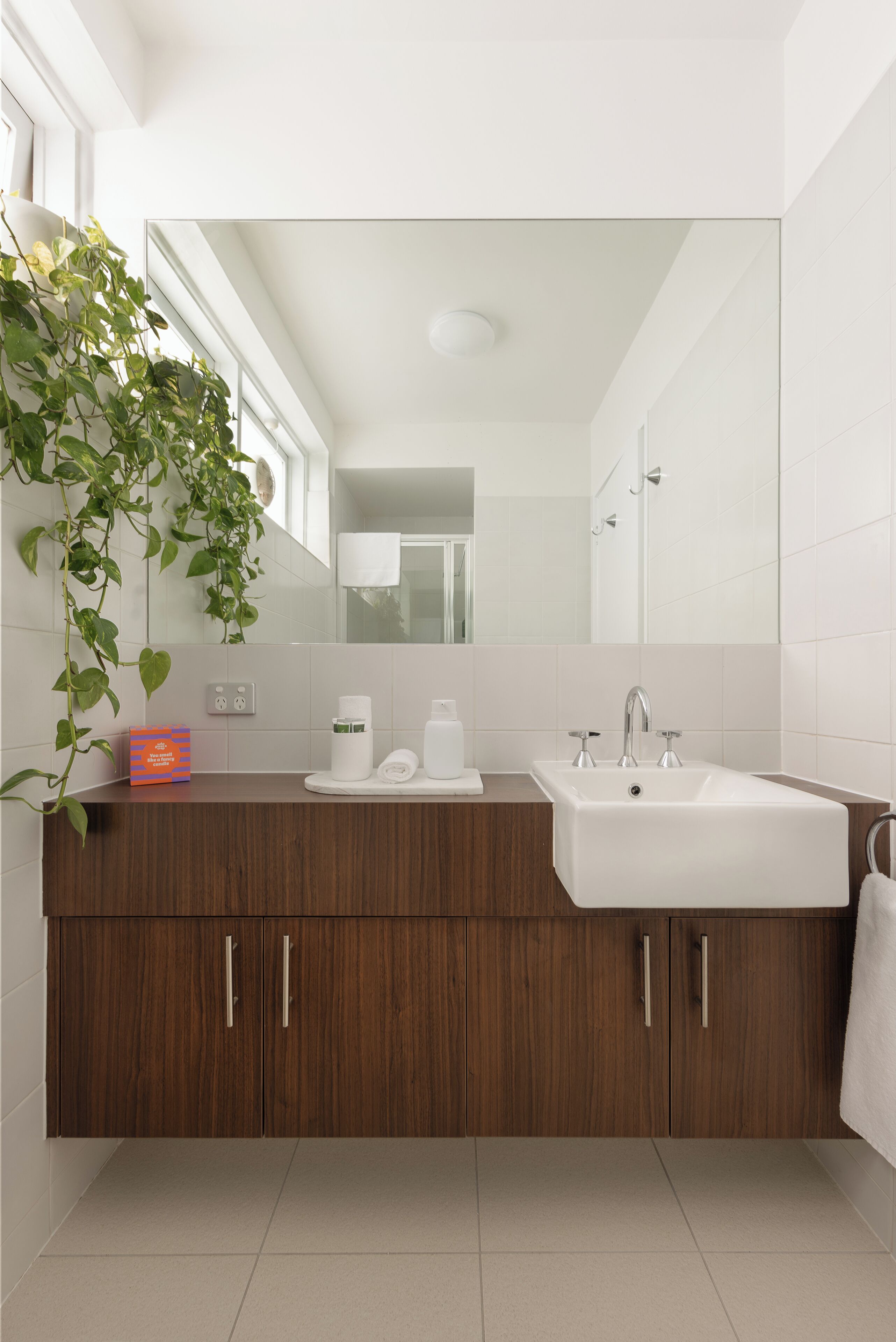 A modern bathroom with a wooden vanity, a large mirror, and a white sink.