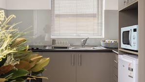 A modern kitchen with a window, built-in appliances, and a dining area. - MAC St Kilda by Melbourne Apartment Collection (St Kilda)