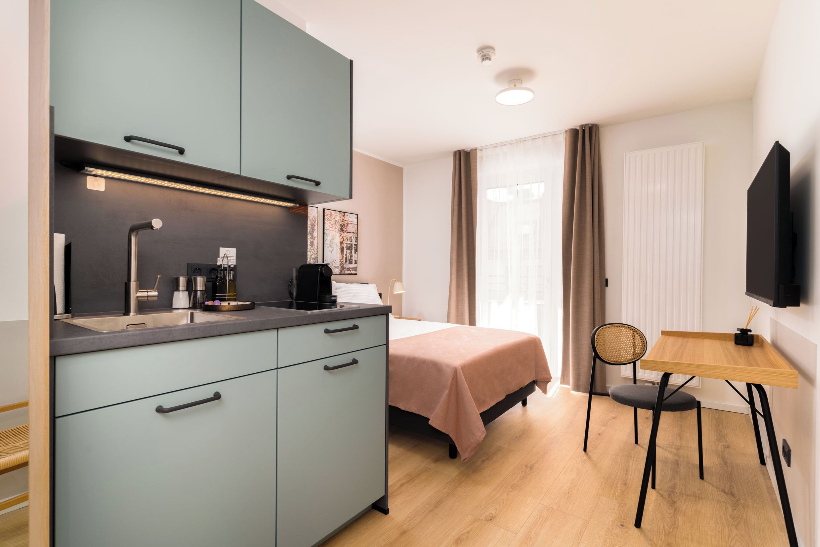A compact bedroom with a bed, bedside table, and a small desk with a chair.