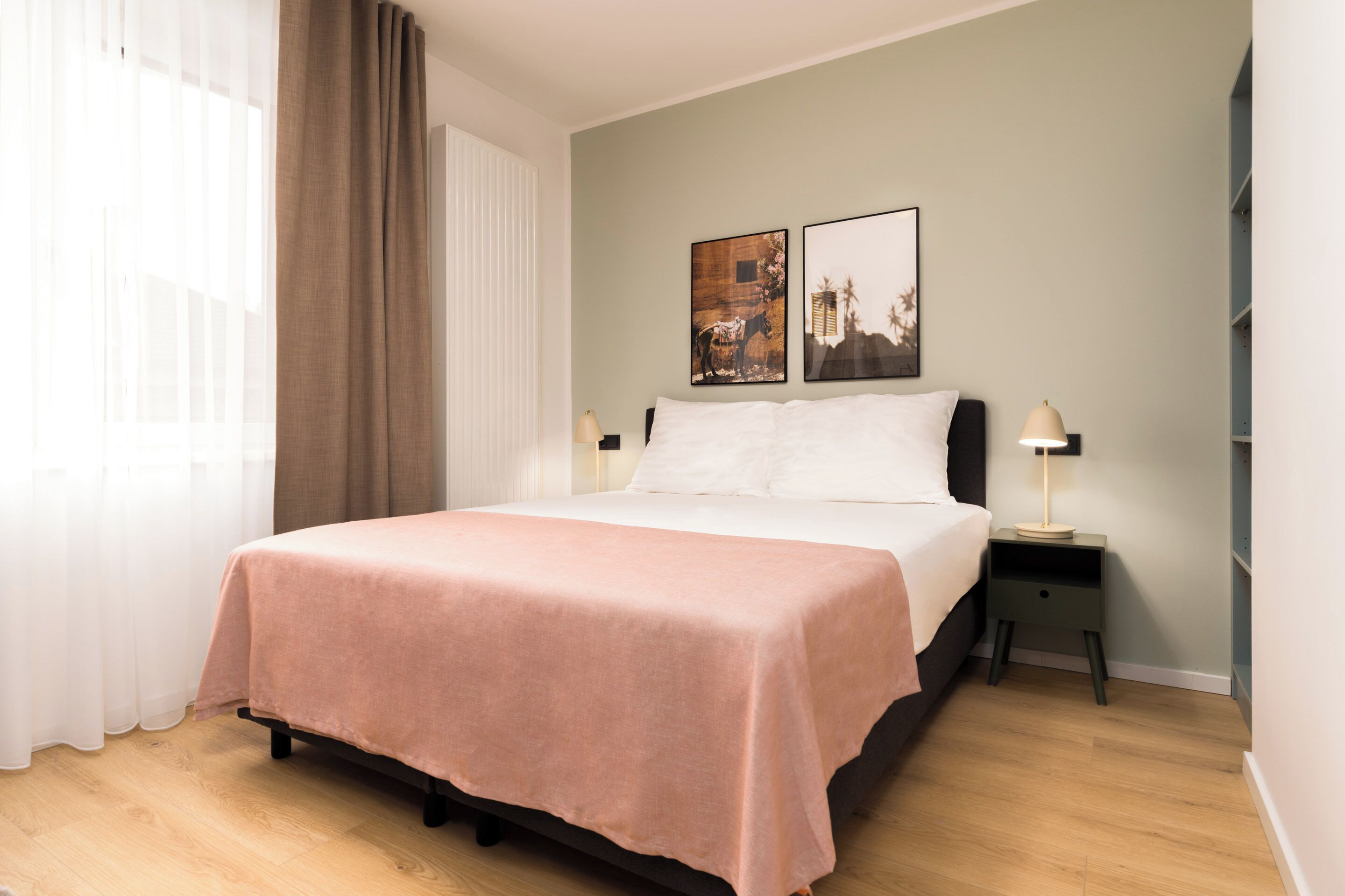 A neatly made bed with a pink bedspread, a bedside table with a lamp, and two framed pictures on the wall.