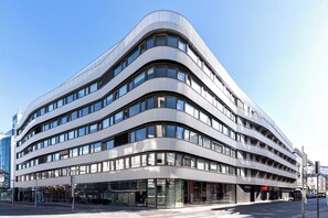 A modern multi-story building with a curved facade, large windows, and a glass entrance. - Limehome Vienna Favoritenstr (Vienna)
