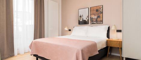 A neatly made bed with a pink bedspread, a bedside table with a lamp, and two framed pictures on the wall.