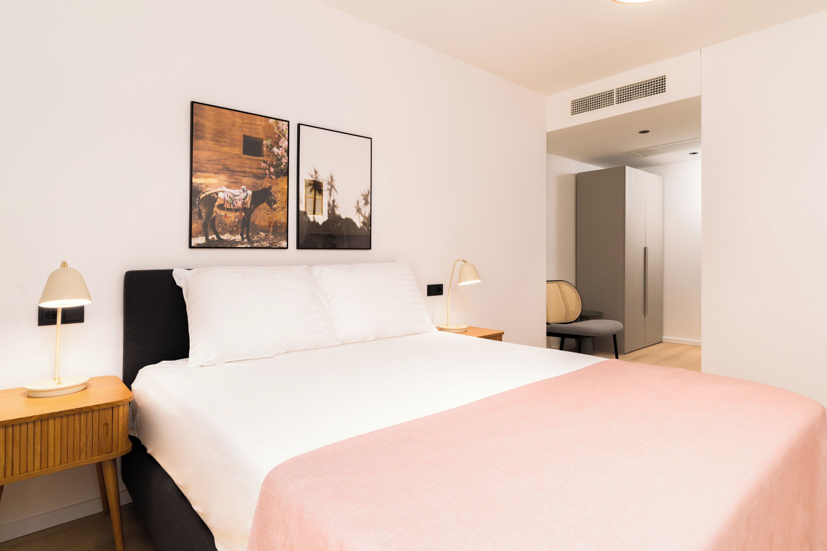 Ein Hotelzimmer mit einem Bett, zwei Nachttischen mit Lampen, einem Sessel und zwei gerahmten Bildern an der Wand.