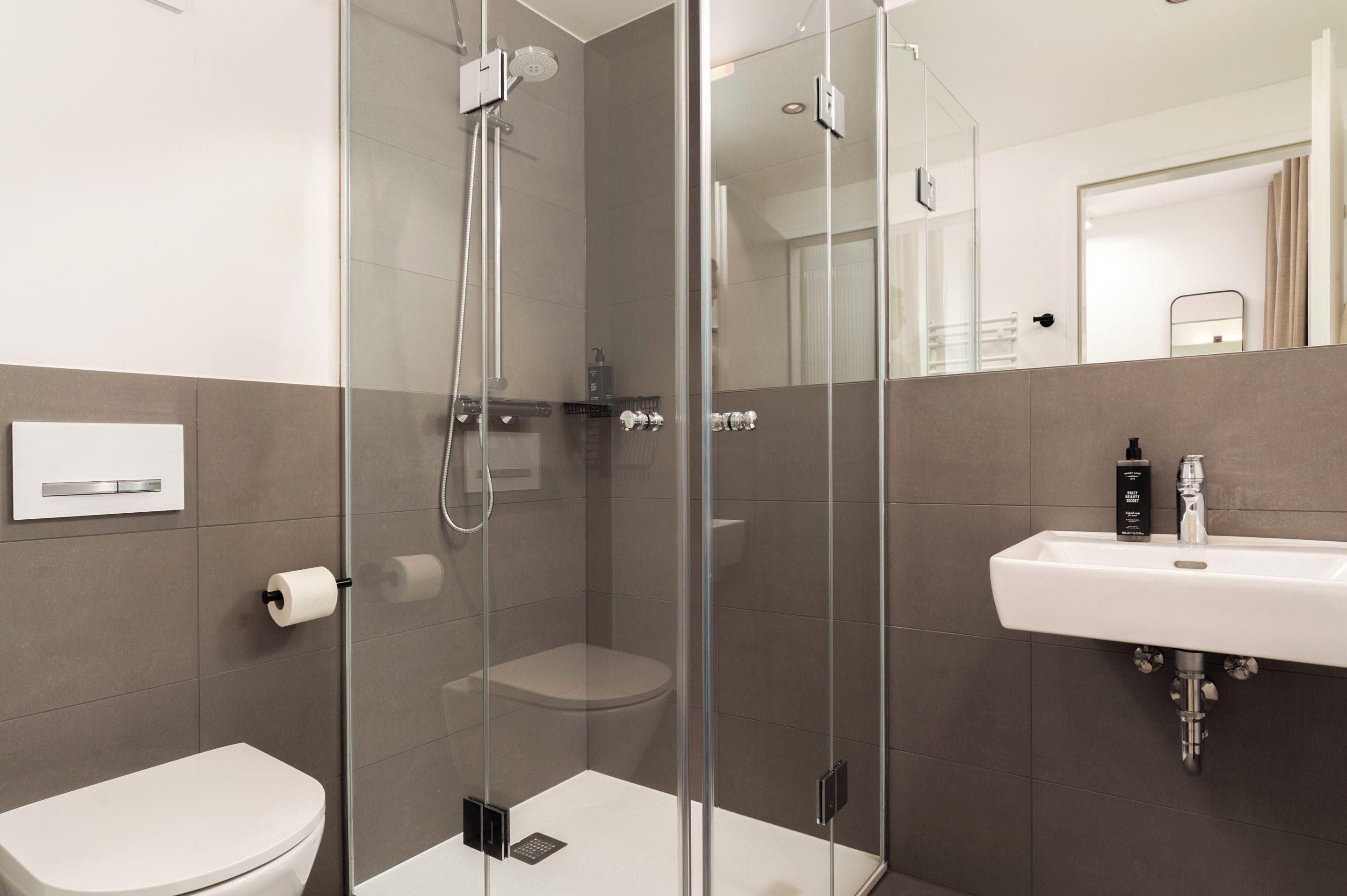 A modern bathroom with a glass-enclosed shower, a white sink, and a toilet.