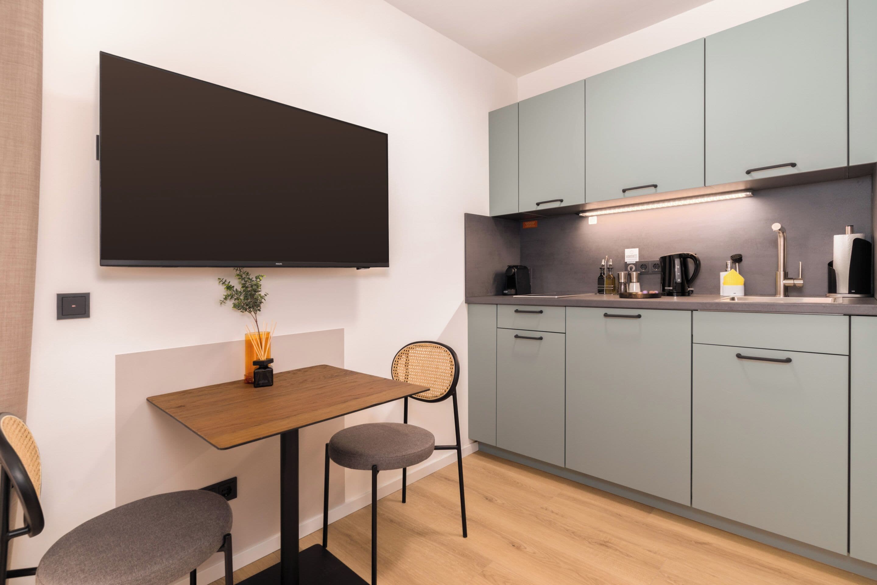 Une cuisine moderne avec des meubles gris, une table en bois et un téléviseur à écran plat fixé au mur.