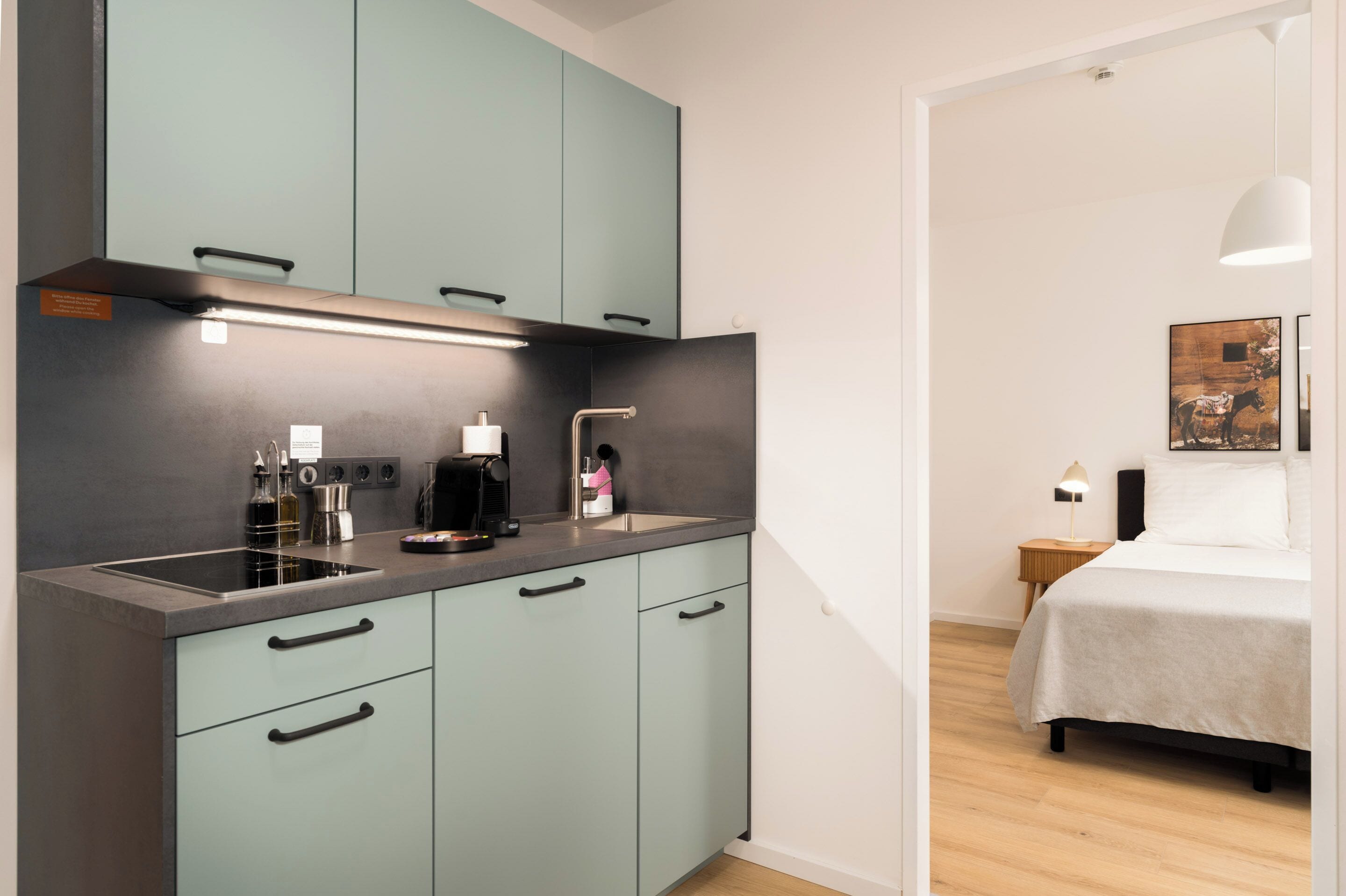 A modern kitchen with teal cabinets, a stainless steel sink, and a countertop with a coffee maker.