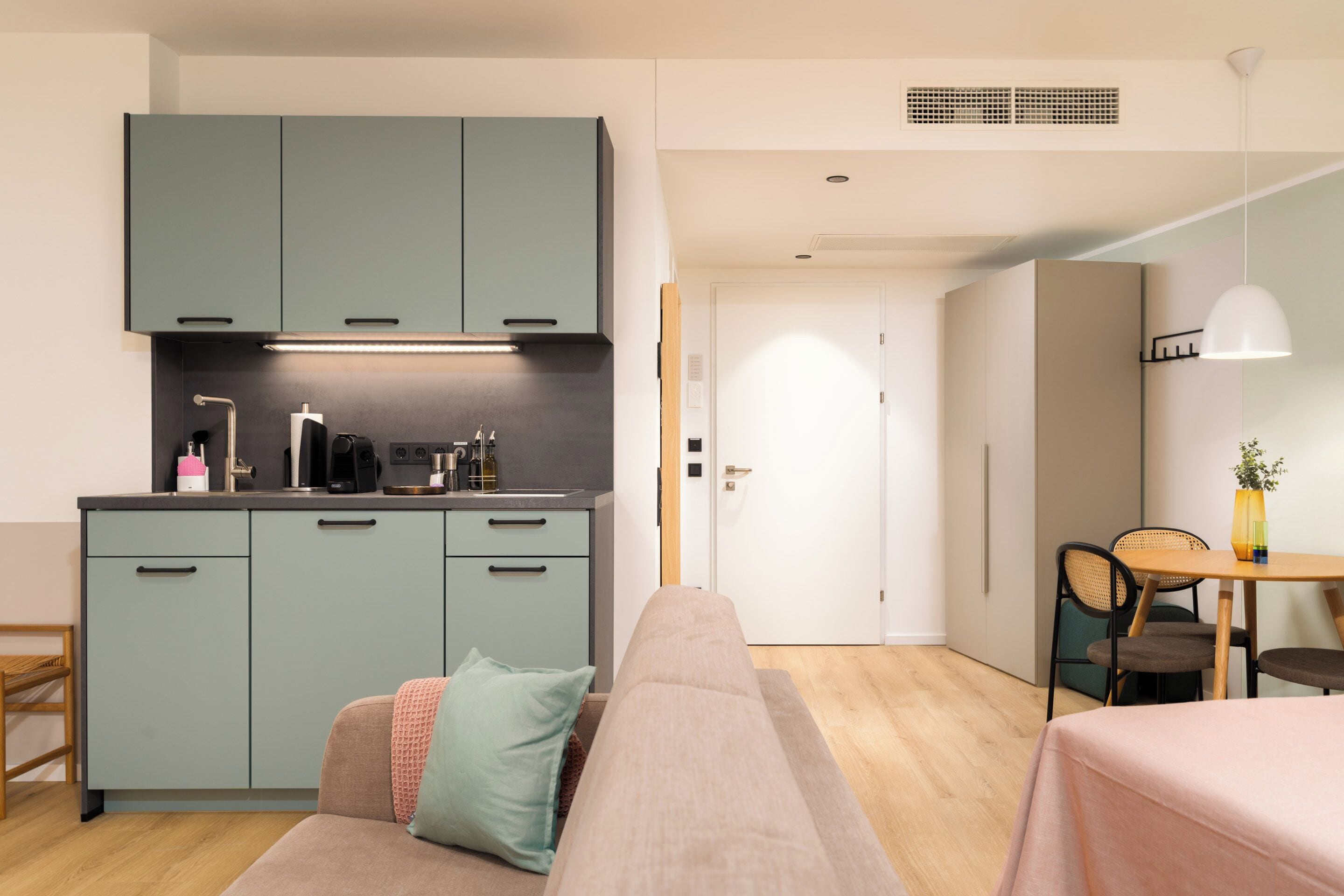 A modern kitchen with teal cabinets, a dining area with a table and chairs, and a cozy seating area with a sofa and cushions.