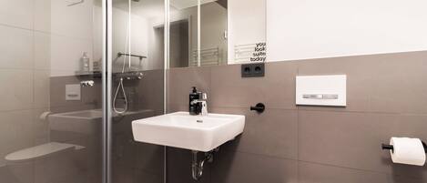 A modern bathroom with a glass shower enclosure, a white sink, and a toilet.