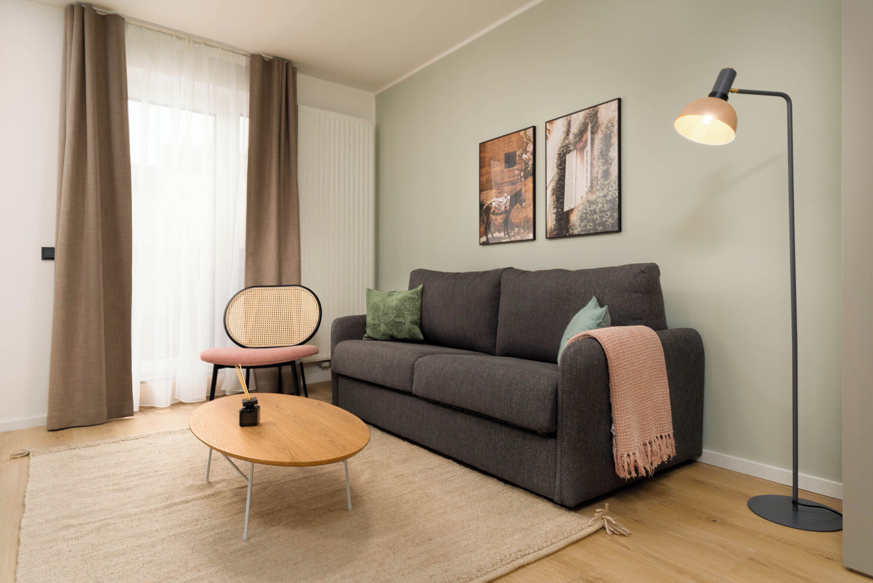 A modern living room with a grey sofa, a round wooden coffee table, a floor lamp, and two framed pictures on the wall.