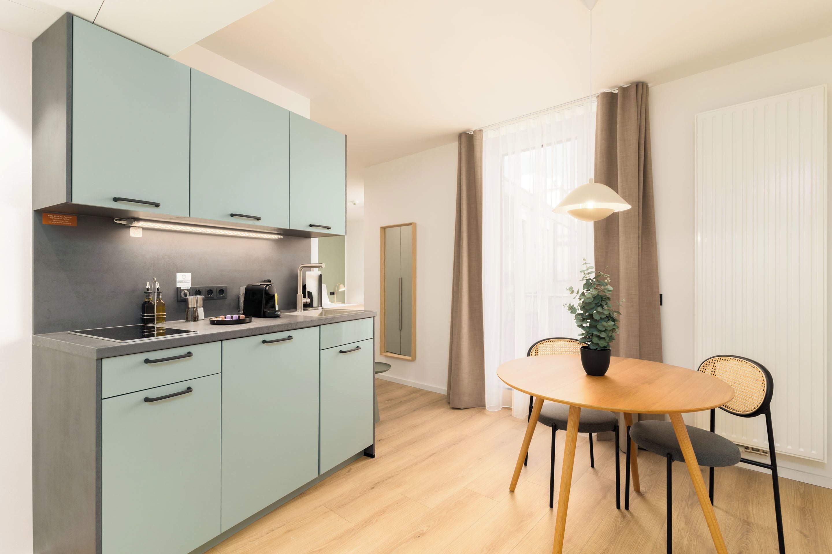 Une cuisine moderne avec des meubles de couleur bleu clair, une table à manger en bois avec deux chaises et une plante en pot.