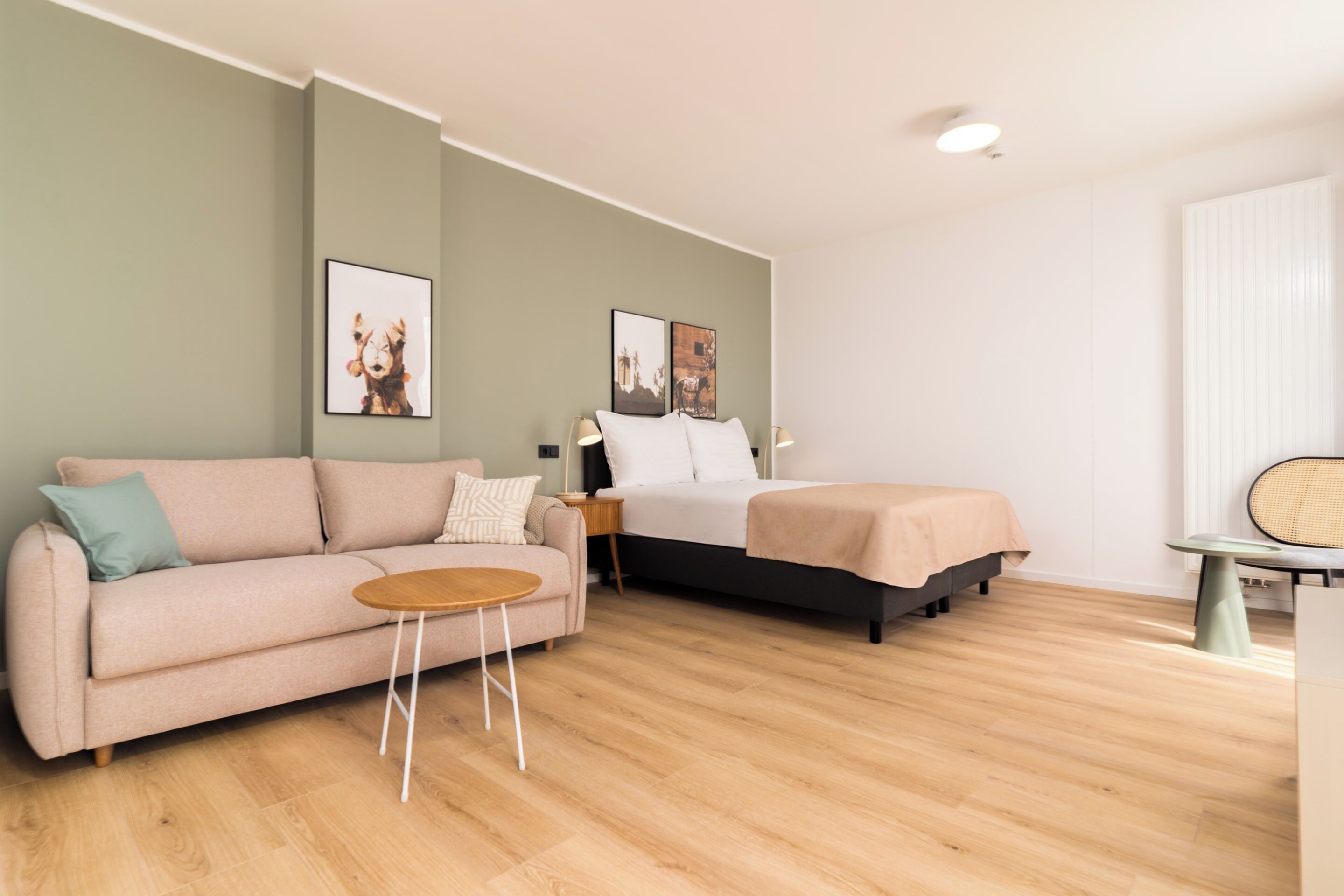 A modern hotel room with a sofa, a bed, a small table, and two framed pictures on the wall.
