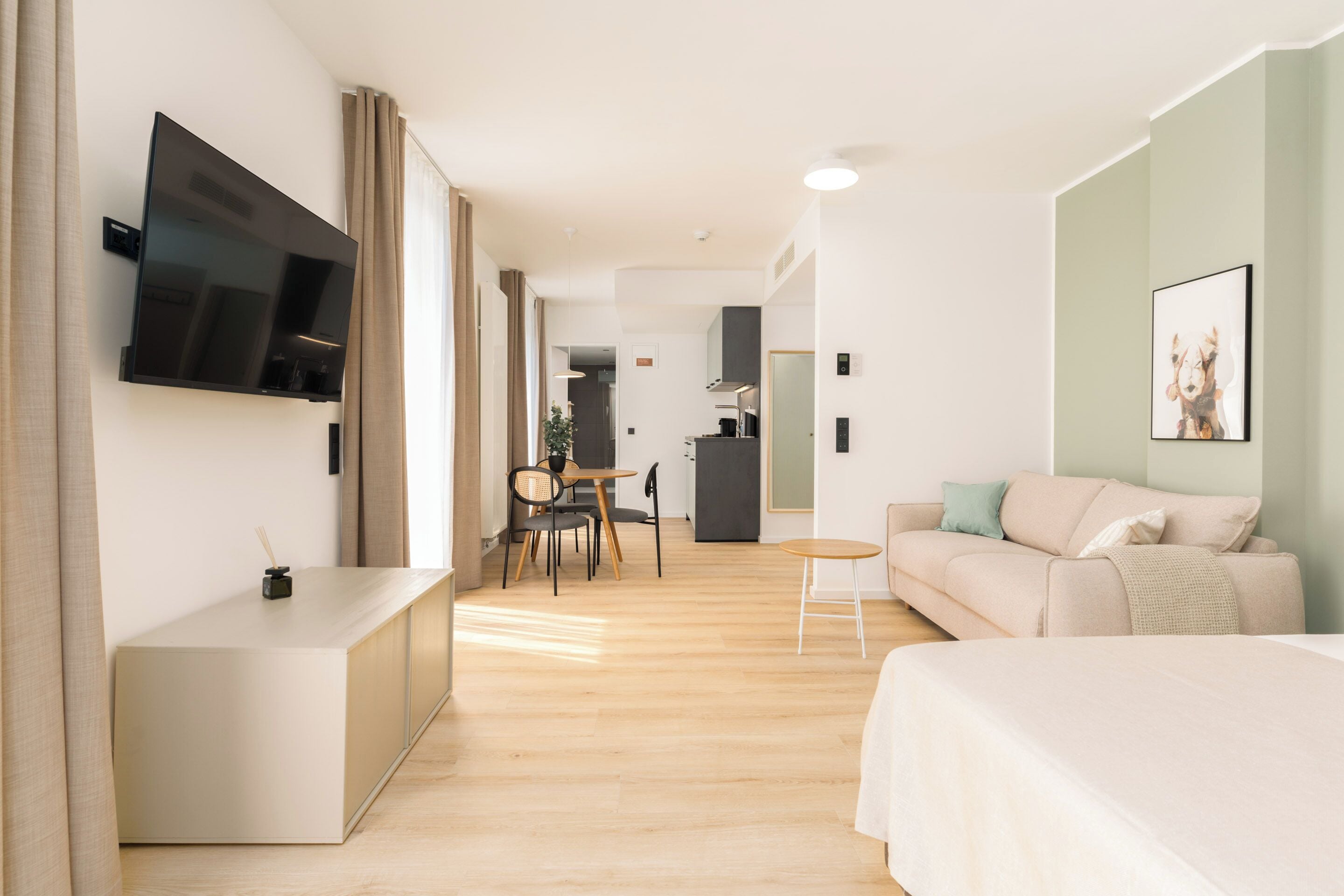 A modern hotel room with a flat-screen TV, a sofa, a bed, a small table, and a desk.