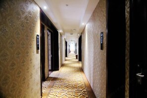 A hotel hallway with patterned carpet and wallpaper, doors, and a light fixture on the ceiling.