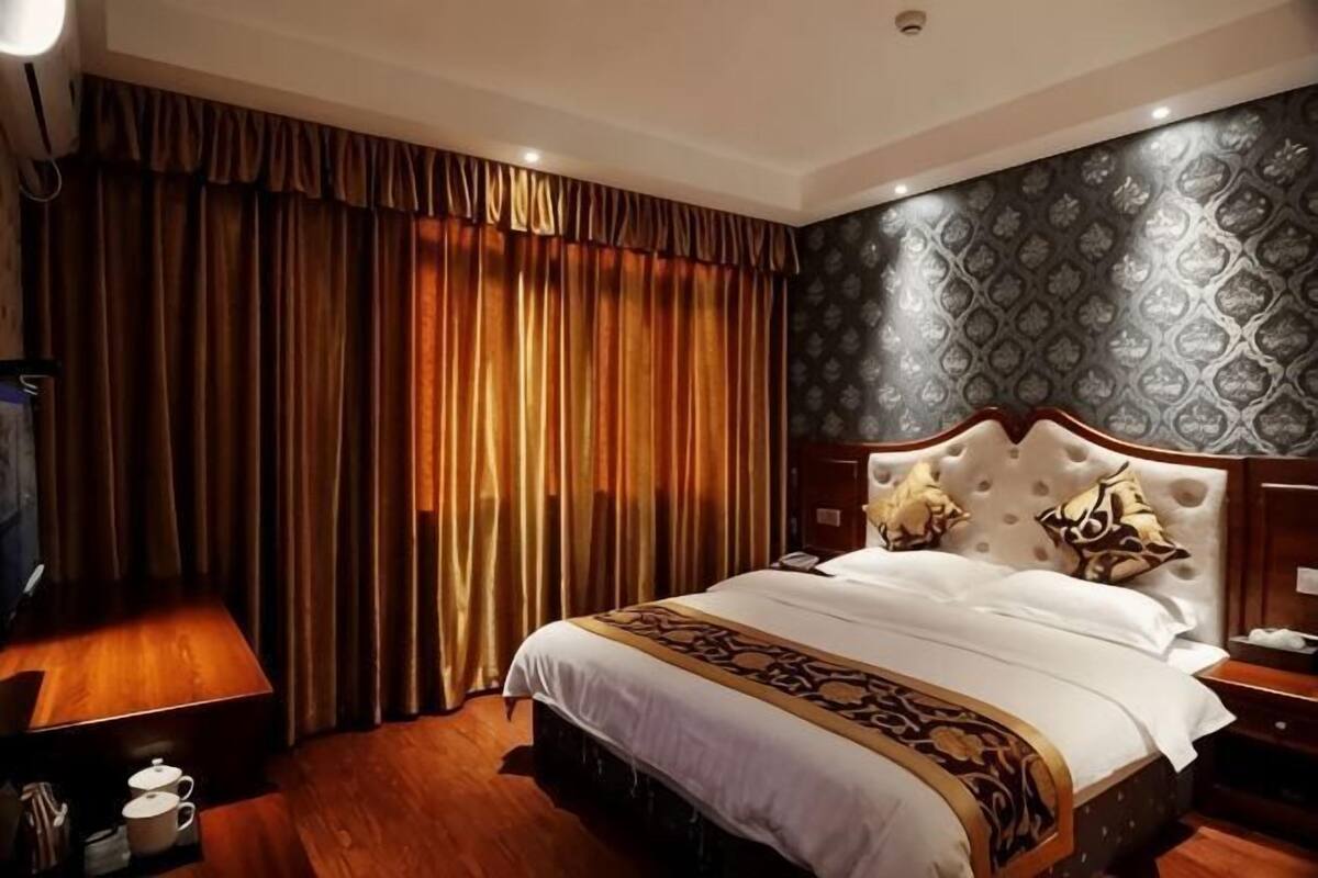 Een hotelkamer met een groot bed, een houten nachtkastje, een nachttafel en een aan de muur bevestigde televisie.